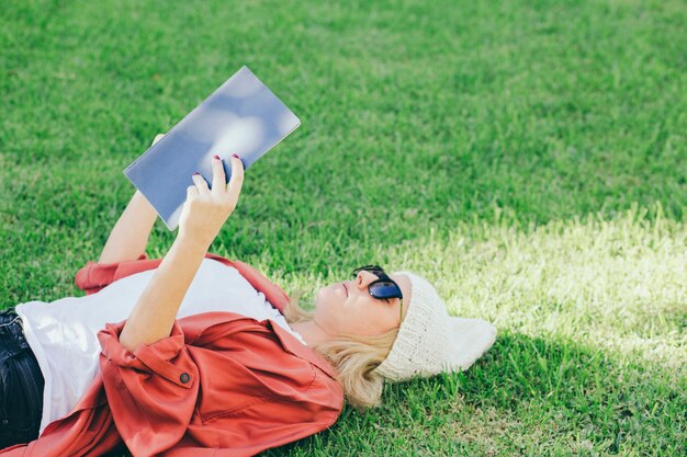 Mujer en gafas de sol que lee el libro en césped