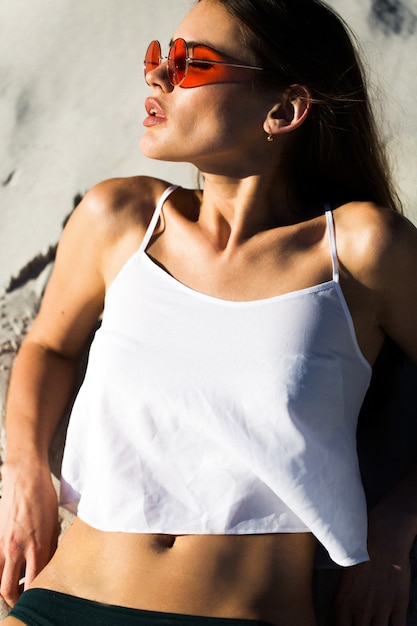 Mujer en gafas de sol rojas se encuentra en una playa blanca