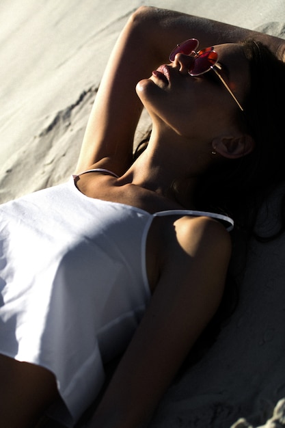 Mujer en gafas de sol rojas se encuentra en una playa blanca