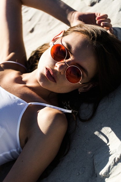 Mujer en gafas de sol rojas se encuentra en una playa blanca