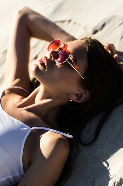 Mujer en gafas de sol rojas se encuentra en una playa blanca