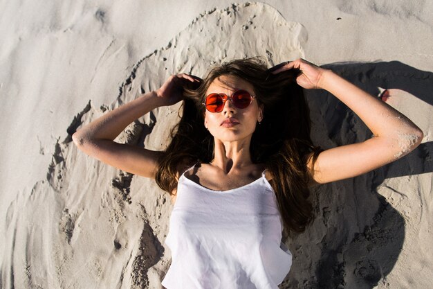 Mujer en gafas de sol rojas se encuentra en una playa blanca