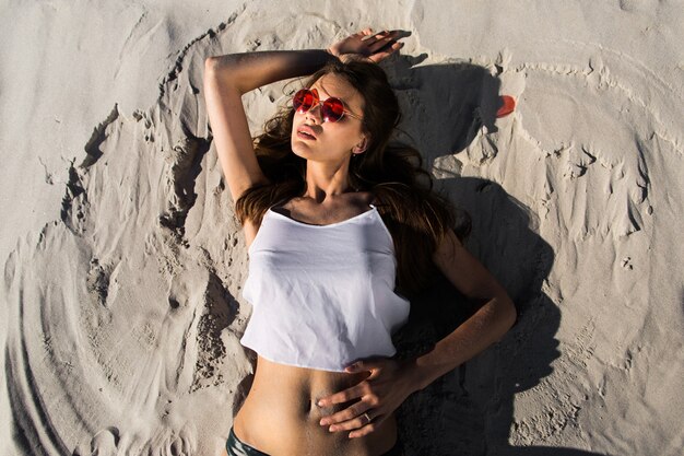 Mujer en gafas de sol rojas se encuentra en una playa blanca