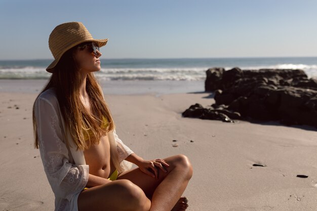 Mujer con gafas de sol y sombrero relajante en la playa