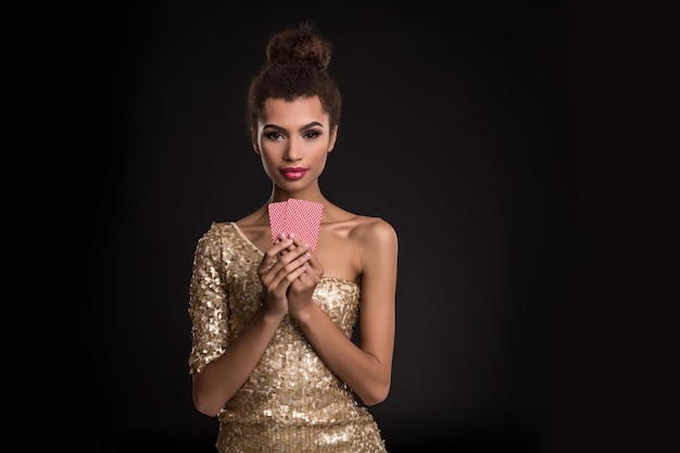 Mujer ganadora: mujer joven con un elegante vestido dorado que sostiene dos cartas, una combinación de cartas de póquer de ases. Foto de estudio sobre fondo negro. emociones