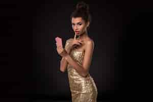 Foto gratuita mujer ganadora: mujer joven con un elegante vestido dorado que sostiene dos cartas, una combinación de cartas de póquer de ases. foto de estudio sobre fondo negro. emociones
