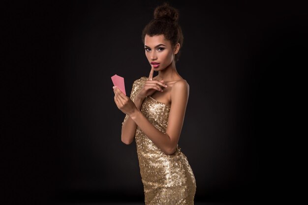 Mujer ganadora: mujer joven con un elegante vestido dorado que sostiene dos cartas, una combinación de cartas de póquer de ases. Foto de estudio sobre fondo negro. emociones