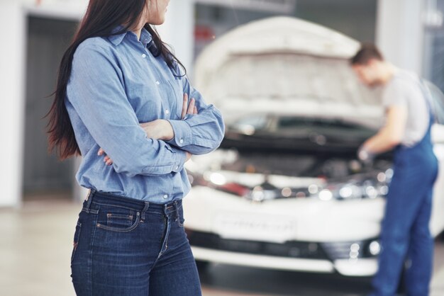 Mujer en un garaje para servicio mecánico. El mecánico trabaja debajo del capó del automóvil.