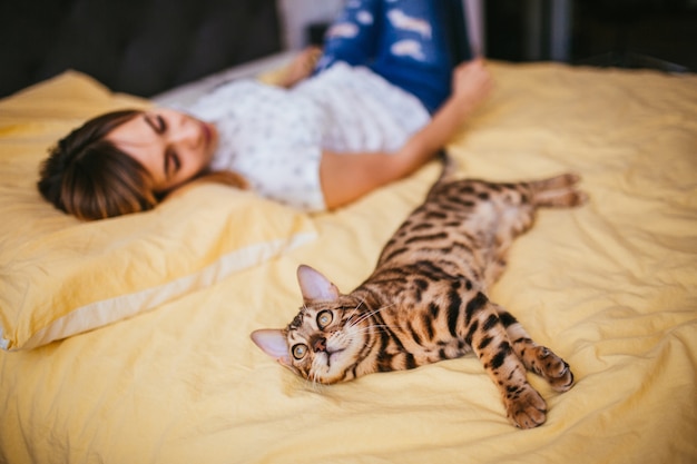 Foto gratuita la mujer y el gato de bengala mienten en la cama