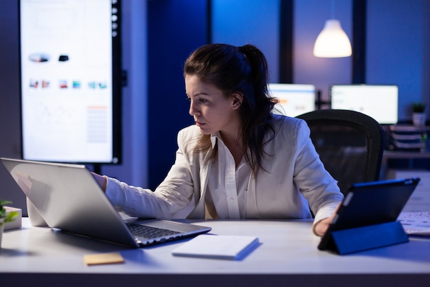 Mujer gerente con laptop y tableta al mismo tiempo trabajando en informes financieros