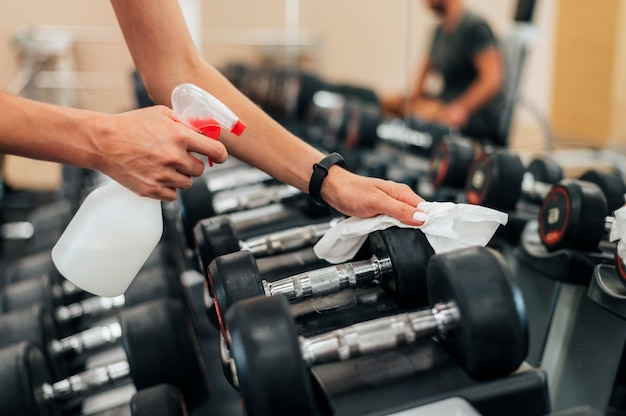 Mujer en el gimnasio desinfectando pesas antes de usarlas