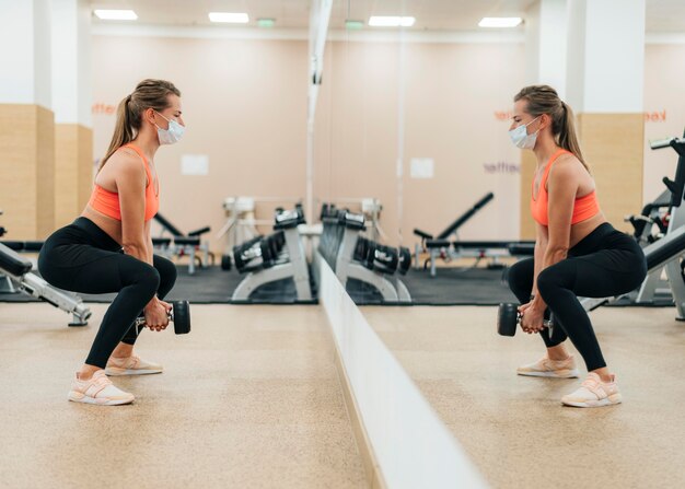 Mujer en el gimnasio entrenando con máscara médica frente al espejo