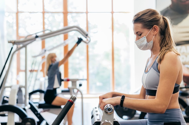 Mujer en el gimnasio con equipo con máscara médica