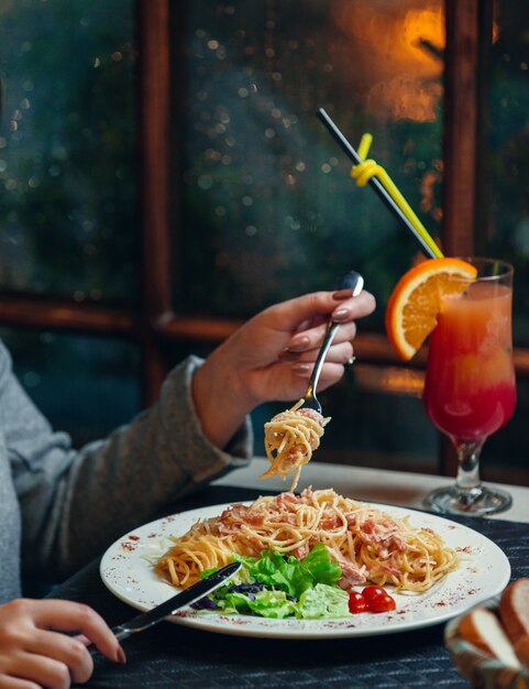 Mujer girando espaguetis con salami de pavo y ensalada fresca en horquilla