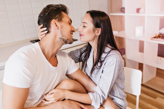 Mujer glamorosa acariciando el cabello del marido, pasando el domingo por la mañana con él