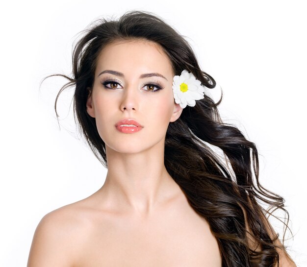 Mujer de glamour hermosa sensualidad con piel limpia y flores en su pelo largo - fondo blanco