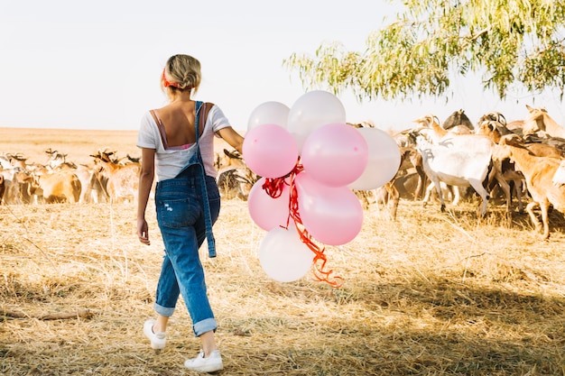 Foto gratuita mujer con globos caminando cerca de manada de cabras