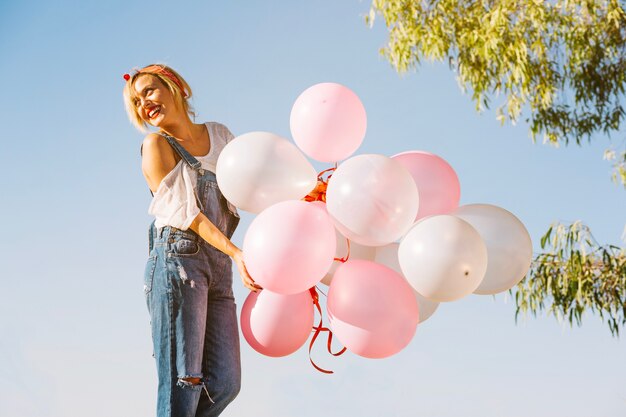 Mujer con globos de pie cerca de un árbol