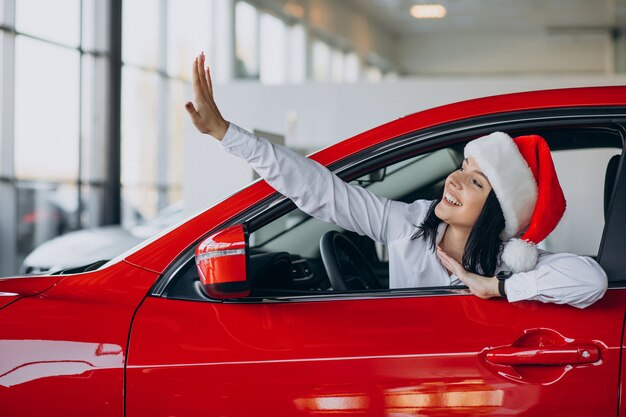 Mujer con gorro de Papá Noel por el coche rojo en una sala de exposición de coches