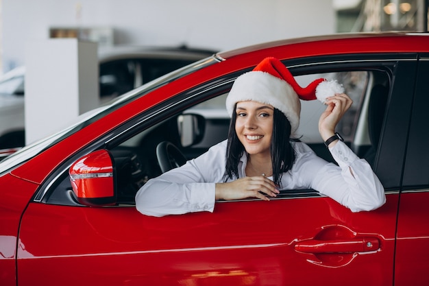 Mujer con gorro de Papá Noel por el coche rojo en una sala de exposición de coches