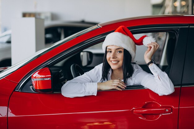 Mujer con gorro de Papá Noel por el coche rojo en una sala de exposición de coches