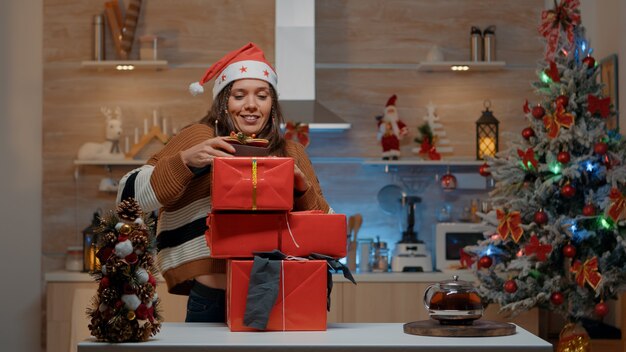 Mujer con gorro de Papá Noel llevando regalos en cocina decorada