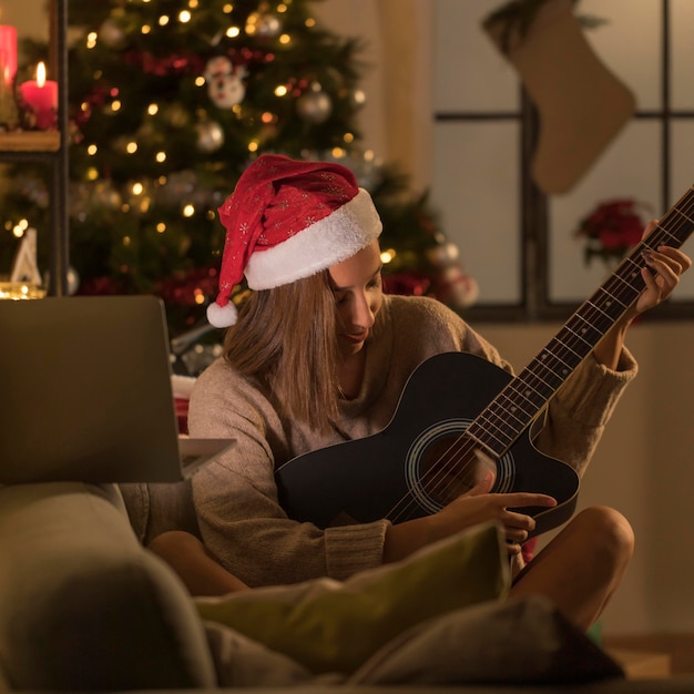 Mujer con gorro de Papá Noel tocando la guitarra delante del portátil