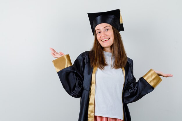 Mujer graduada extendiendo las palmas hacia los lados en ropa casual, uniforme y mirando alegre, vista frontal.