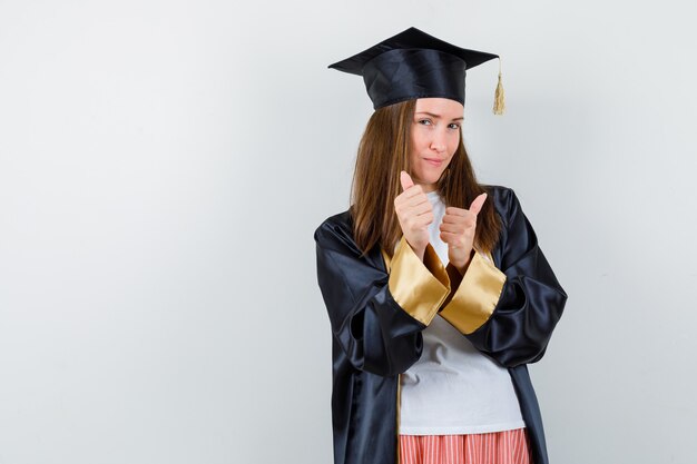 Mujer graduada mostrando doble pulgar hacia arriba en ropa casual, uniforme y confiada. vista frontal.