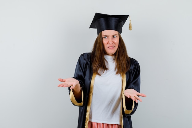 Mujer graduada mostrando gesto de impotencia en ropa casual, uniforme y mirando confundido, vista frontal.