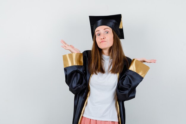 Mujer graduada mostrando gesto de impotencia en ropa casual, uniforme y mirando confundido, vista frontal.