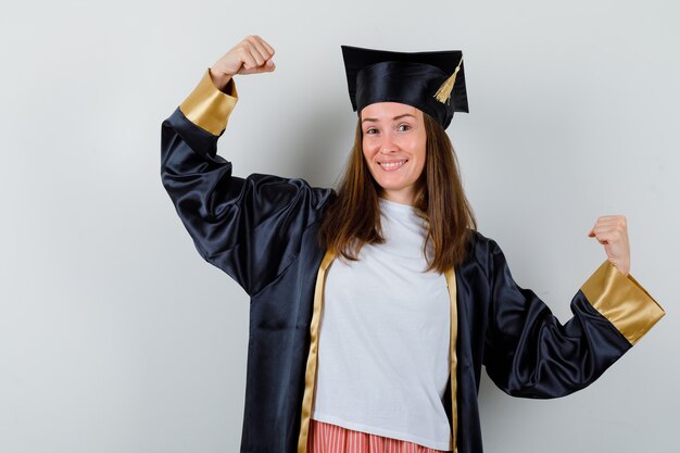 Mujer graduada que muestra el gesto del ganador en ropa casual, uniforme y alegre. vista frontal.