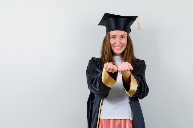 Mujer graduada en ropa casual, uniforme haciendo gesto de recibir o dar y mirando alegre, vista frontal.