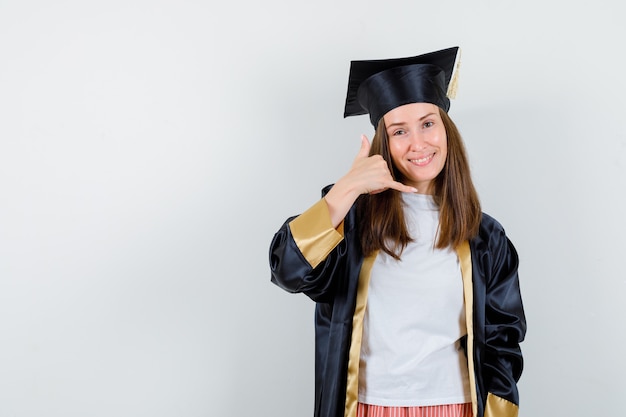 Mujer graduada en ropa casual, uniforme mostrando gesto de teléfono y mirando confiado, vista frontal.