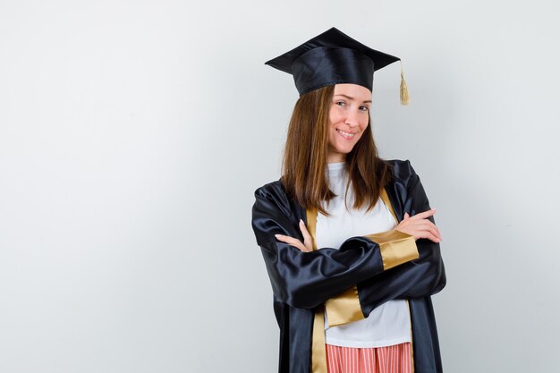 Mujer graduada en ropa casual, uniforme de pie con los brazos cruzados y mirando confiada, vista frontal.