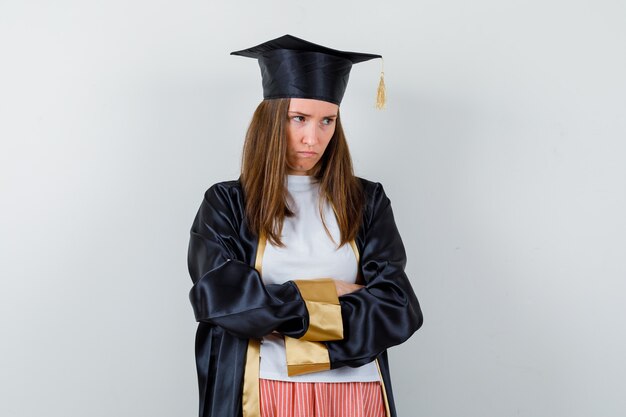 Mujer graduada en ropa casual, uniforme de pie con los brazos cruzados y mirando triste, vista frontal.