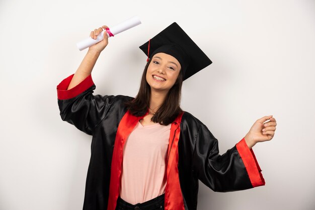 Mujer graduada universitaria en vestido de pie sobre fondo blanco.