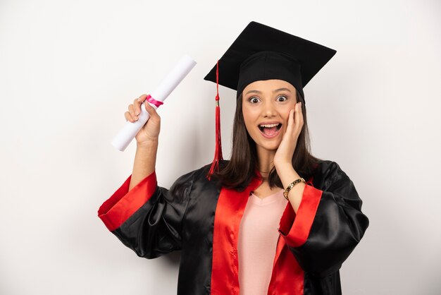 Mujer graduada universitaria en vestido sintiéndose feliz sobre fondo blanco.