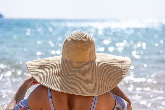 Una mujer con un gran sombrero toma el sol en la playa cerca del mar.