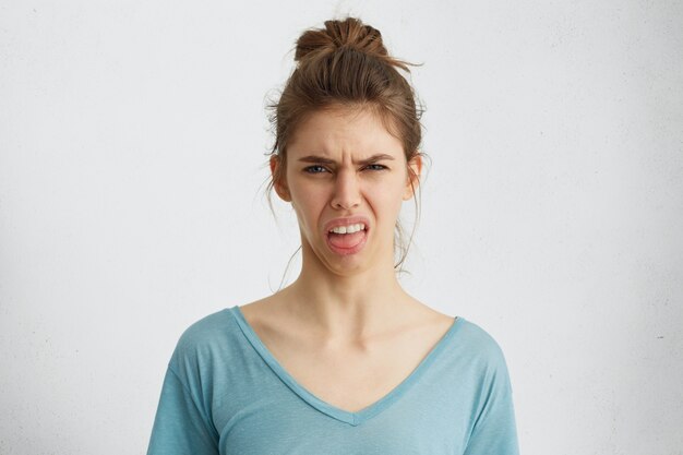 Mujer gruñona mostrando su disgusto mientras fruncía el ceño con insatisfacción mostrando su lengua.