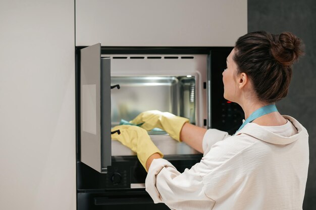 Una mujer con guantes amarillos limpiando el horno.