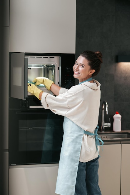 Una mujer con guantes amarillos limpiando el horno.