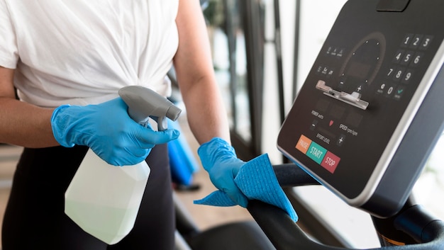 Foto gratuita mujer con guantes de limpieza de equipos de gimnasio con solución