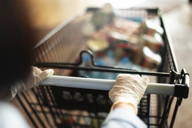 Mujer con guantes para prevenir el coronavirus mientras usa un carrito de compras