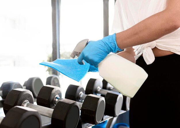 Mujer con guantes y solución de limpieza desinfectante de equipos de gimnasio