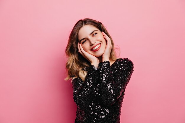 Mujer guapa complacida posando con sonrisa sincera. Retrato de interior de linda chica europea aislada en la pared rosa.