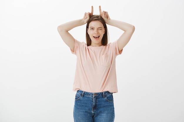 Mujer guapa descarada mostrando cuernos sobre la cabeza y guiñando un ojo feliz