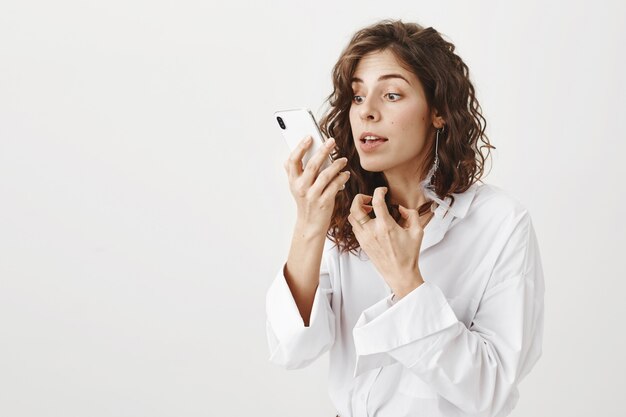 Mujer guapa elegante control de maquillaje en la cámara de su teléfono inteligente