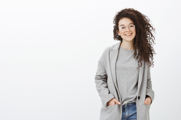 Mujer guapa de moda en gafas y elegante abrigo, tomados de la mano en el bolsillo, sonriendo ampliamente