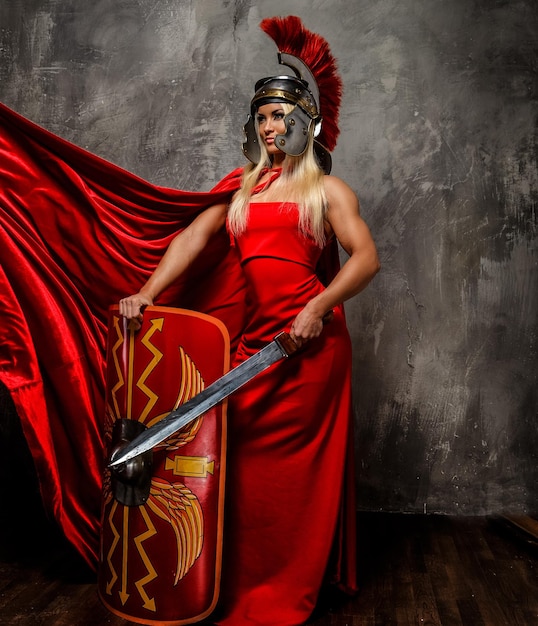 Foto gratuita mujer guerrera romana con vestido rojo que revolotea sostiene espada y escudo.